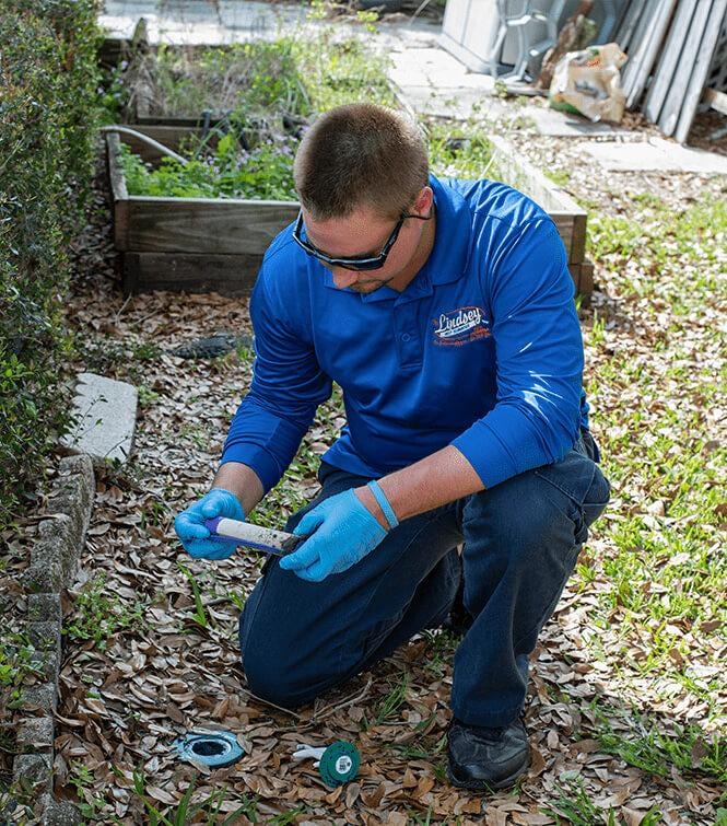 a technician checking a termite baiting trap outside of a jacksonville florida home