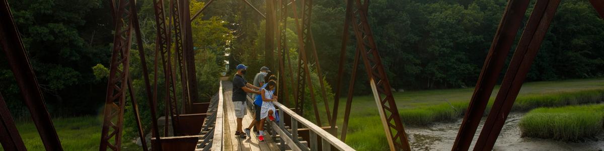 A family looks out at a wetland from an iron and wood bridge