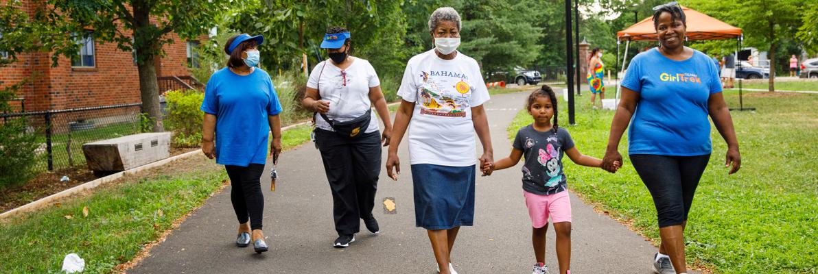 Four women and a girl walk on a paved trail
