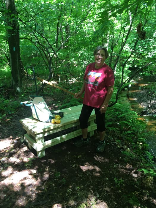 a trail worker next to a newly constructed wooden bench (Credit: Linda Anderson)