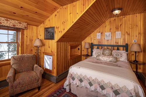 A bed, chair, mini-fridge, and lamp in a wood paneled room