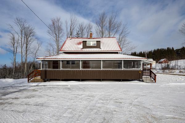 A snow covered house with a red roof and brown paint