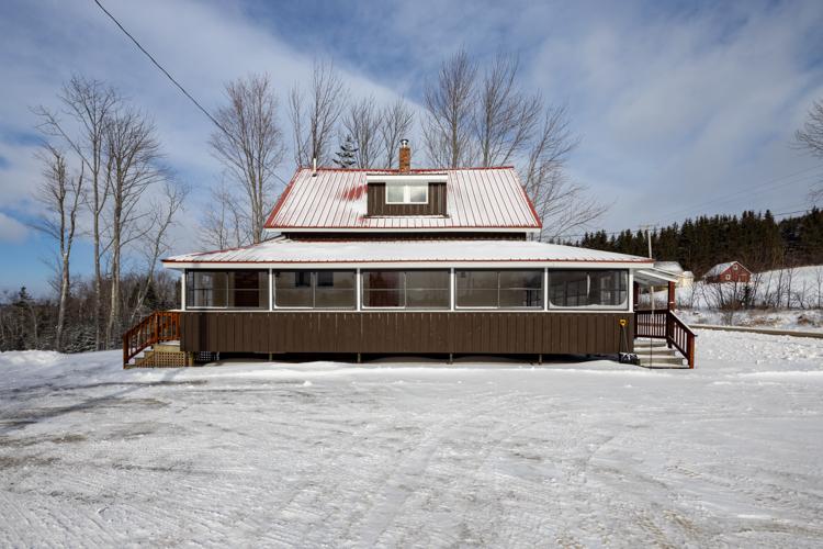 A snow covered house with a red roof and brown paint