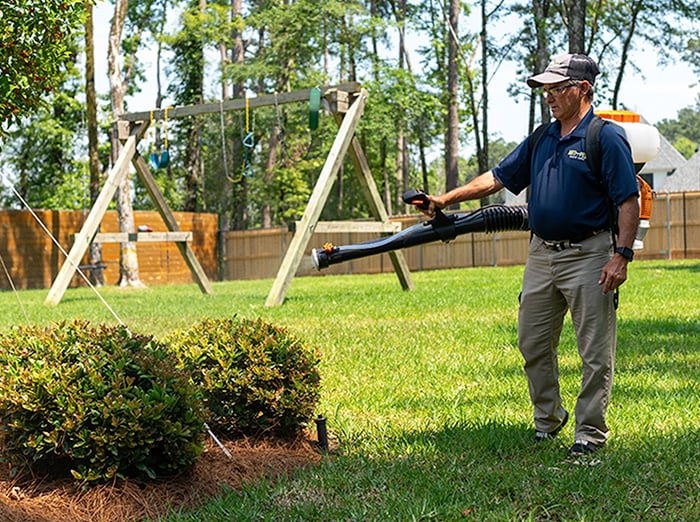 anti-pest tech treating around shrubs and trees for mosquitoes