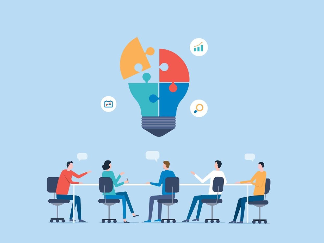 Cartoon People sitting around a table wit a lightbulb above