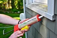 A person caulking around a window from outside