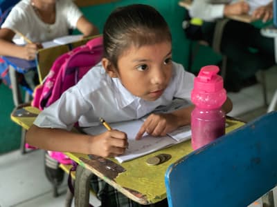 Student listens intently as her teacher writes on the chalk board.