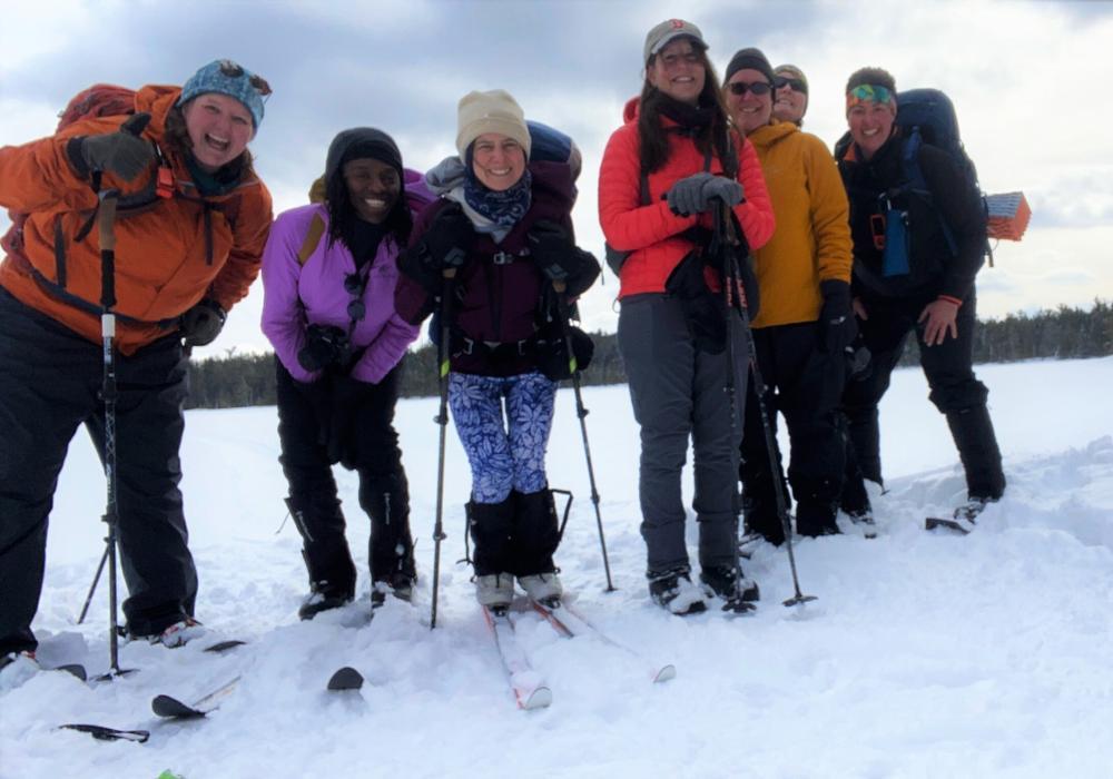 A group of women pause skiing &amp; snowshoeing to smile at the camera