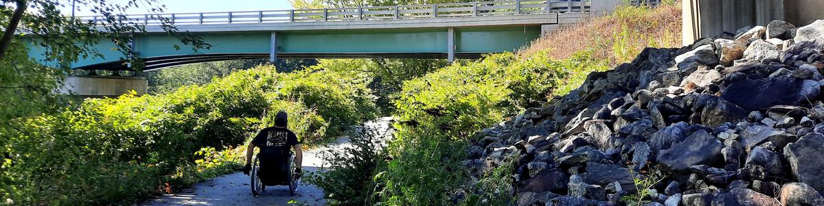 A man in a wheelchair crosses under a bridge