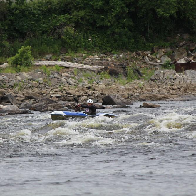 A kayaker paddles over a wave caused by a rapid