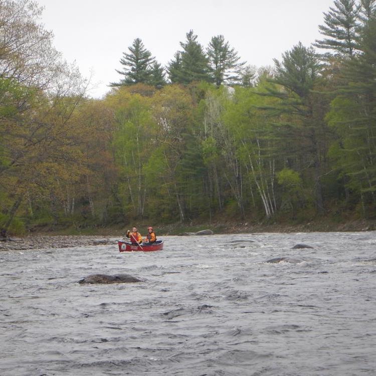 Two people paddle a canoe through a riffle on a wide river