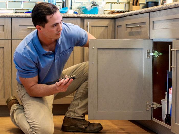 pest control technician checking for rodent activity under kitchen sink