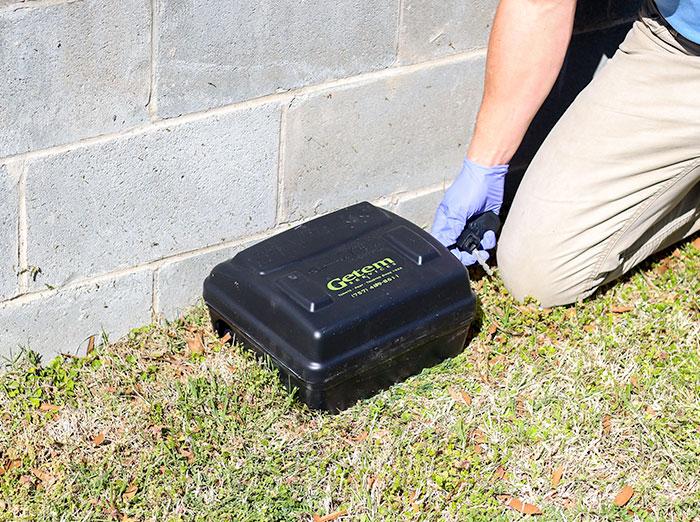 getem services pest control tech checking rodent bait station outside rental