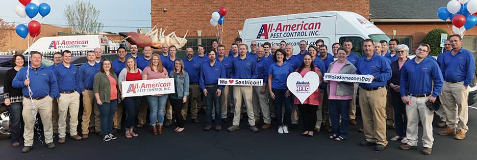 the all-american pest control team standing in front of a company van with signs to celebrate the second annual hometown hero award