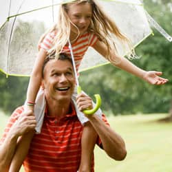 family playing outside in the rain with an umbrella