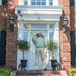technician removing spider webs outside a home