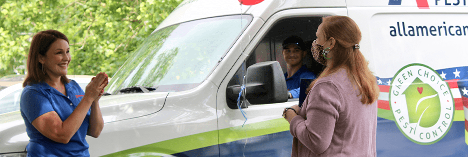 the all-american pest control team standing in front of a company van with signs to celebrate the second annual hometown hero award