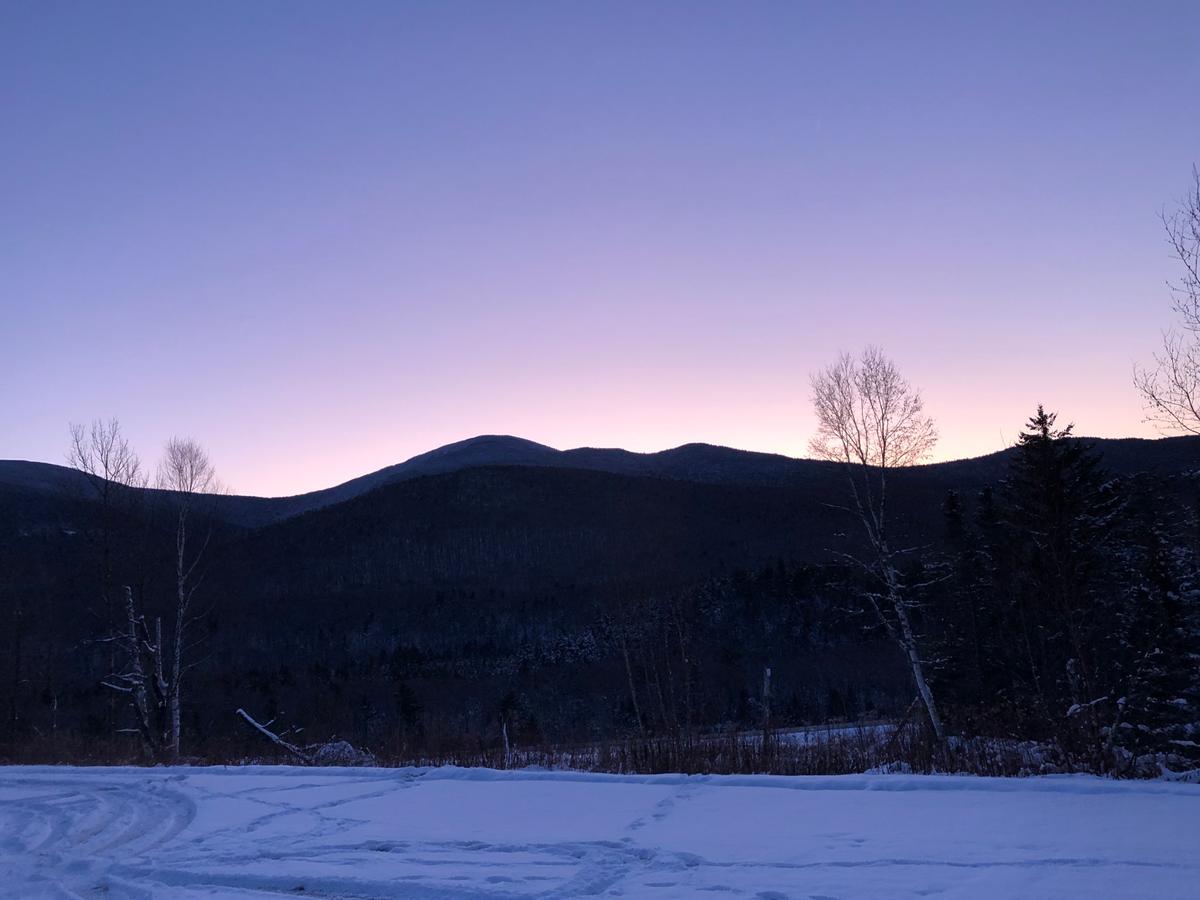 A clear, purple and pink sky behind a silhouette of a mountain ridge