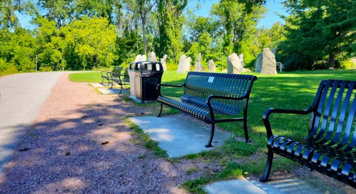 Benches lining a paved walkway, with waste barrels and mowed grass behind