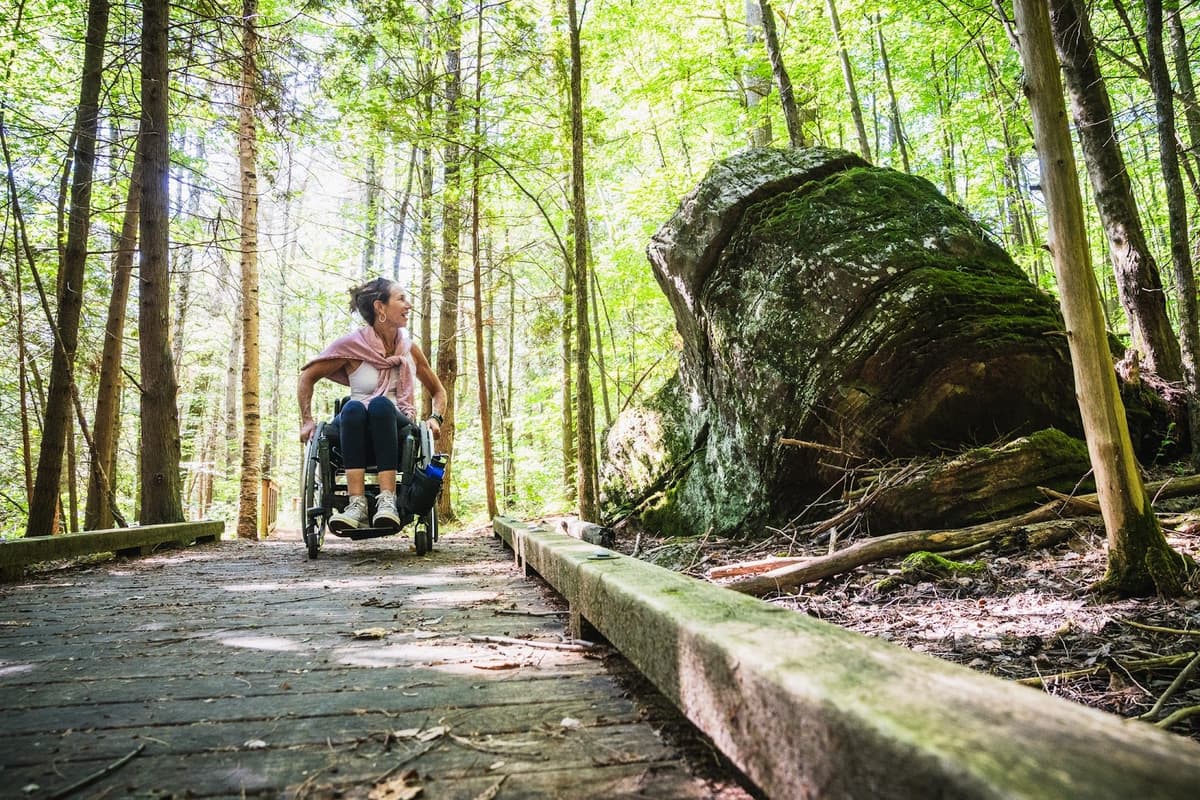 Woman in her wheelchair on a boardwalk through the woods enjoying the scenery