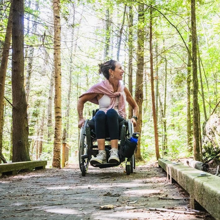Edie in her wheelchair on a boardwalk through the woods enjoying the scenery