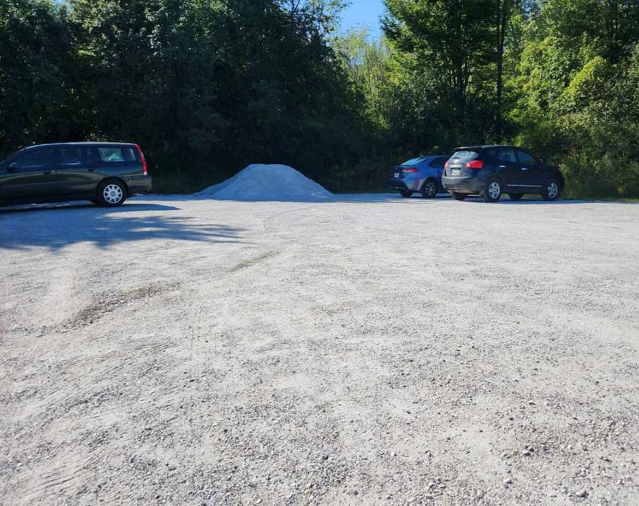 Flat, gravel surface of parking lot, with three cars parked in the background